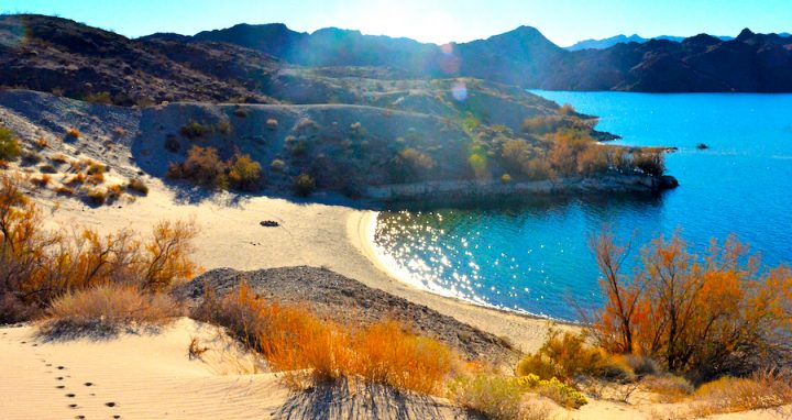 Beach on a desert lake with mountains in the background during sunset.