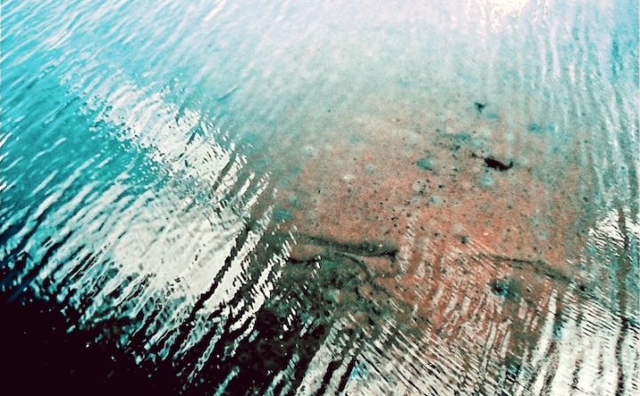 Blue water with a transparent spot showing the ground below the water.