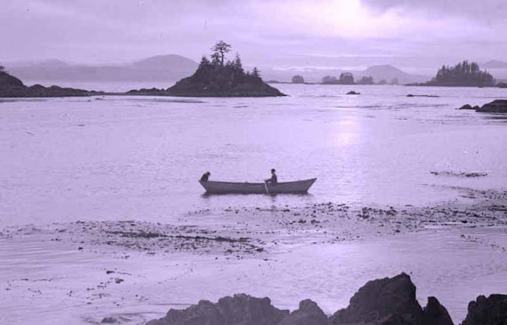 Old black and white photograph of a person in a canoe in Alaskan waters.
